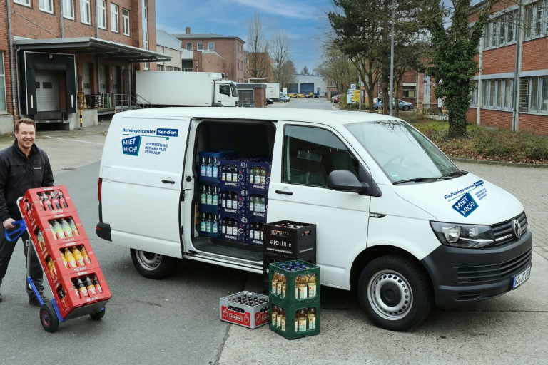 Lieferwagen mit Getränkekisten, Fahrer zieht eine Palette mit Flaschen.